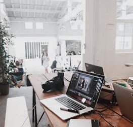 A bright, modern workspace featuring laptops, a camera, and a drawing tablet in an indoor office.